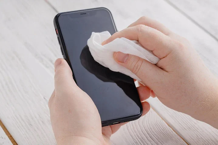 a person cleaning a smartphone screen with a white cloth or wipe