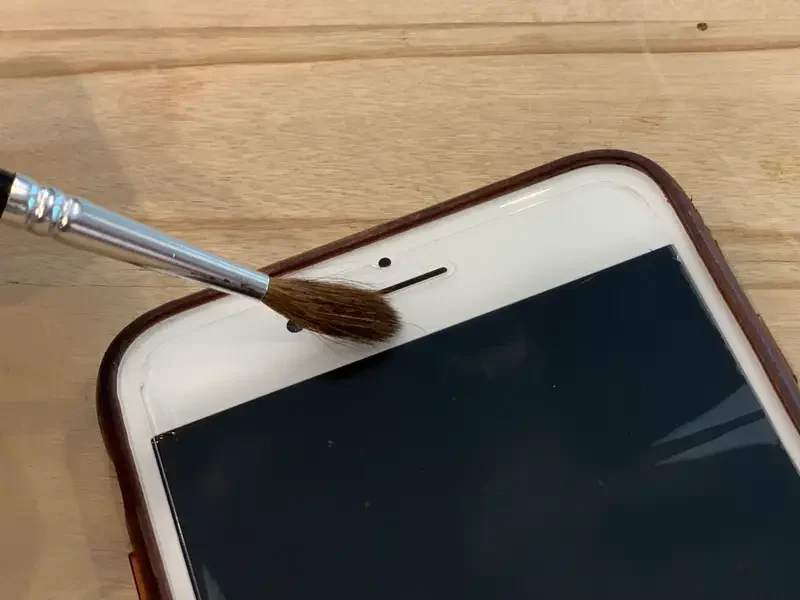 person cleaning the earpiece speaker on an iPhone with a small brush