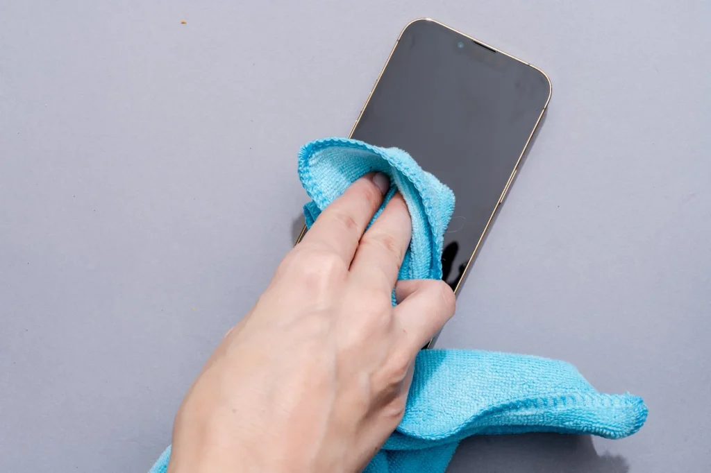  a hand using a microfiber cloth to clean the screen of a smartphone